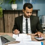 A focused businessman works with a calculator and documents in a modern office.